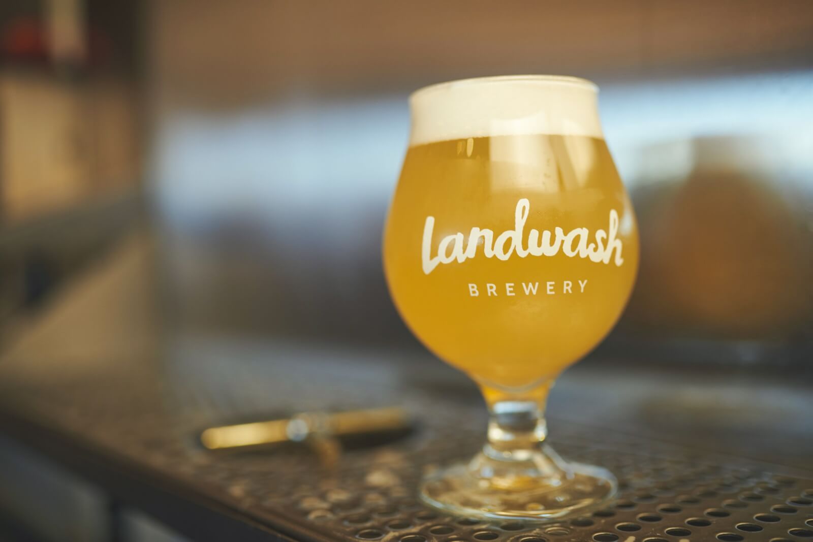 Full glass of Landwash Brewery craft beer sits on the bar top.