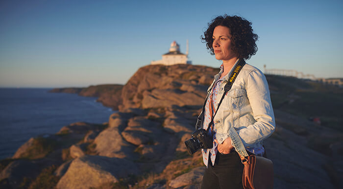 Photo of a woman looking out to sea in the foreground and lighthouse in background