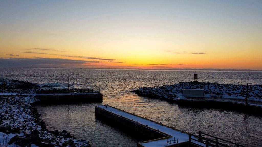 A sunset view from the wharf at Bauline overlooking the ocean. The wharf itself, and the ground, are covered with a dusting of snow.