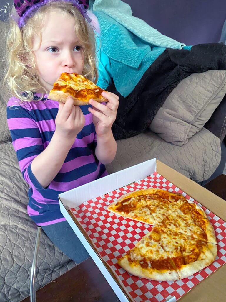 An adorable little girl eating a slice of Yellowbelly pizza. The rest of the pizza sits in a takeout box.