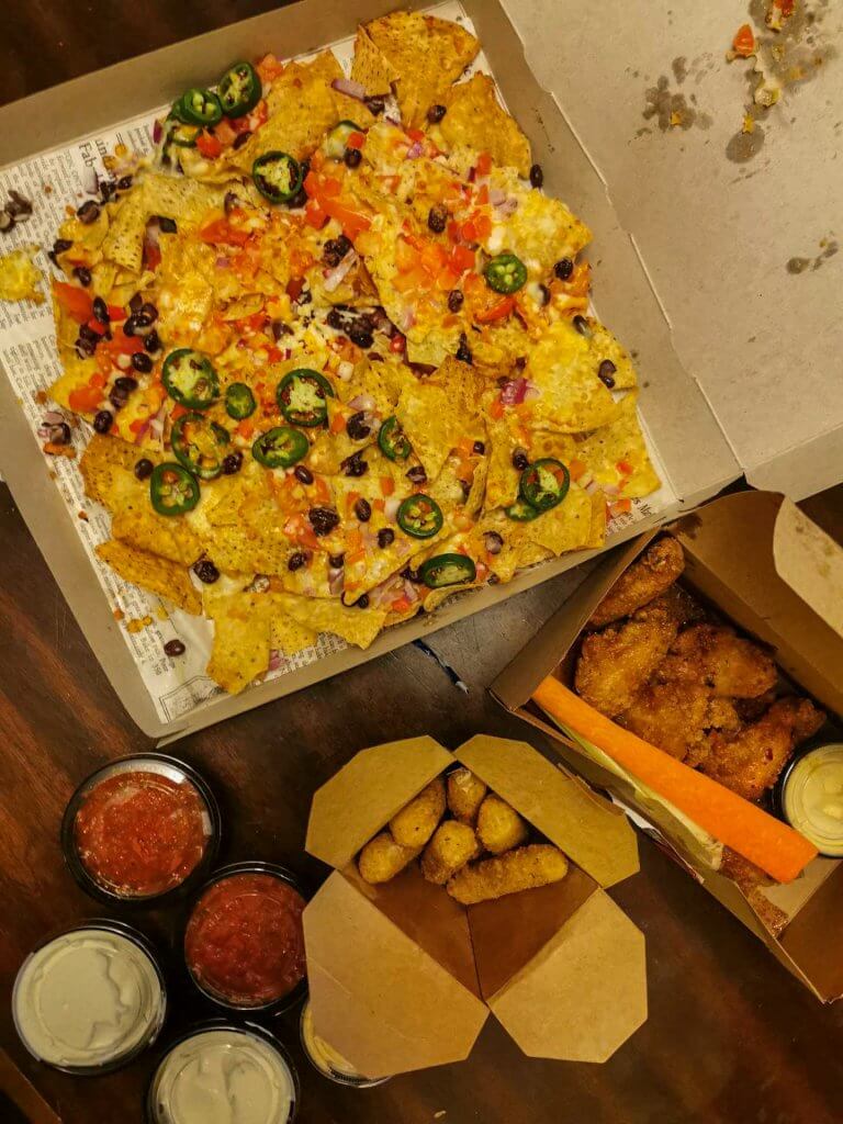 A table is filled with nachos, mozza sticks, and wings with multiple dipping sauces on the side.
