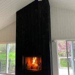 Photo of a simple black fireplace against a backdrop of white shiplap walls and ceiling as well as extensive windows